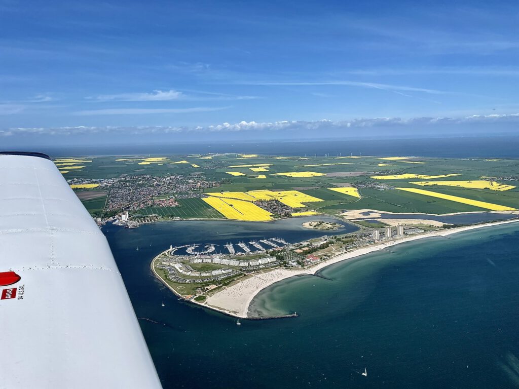 Blick auf die Insel Fehmarn während der Rapsblüte aus einem Flugzeug fotografiert. Der Rundflug über Fehmarn ist gerade über der Ostsee und die Tragfläche ist zu sehen.