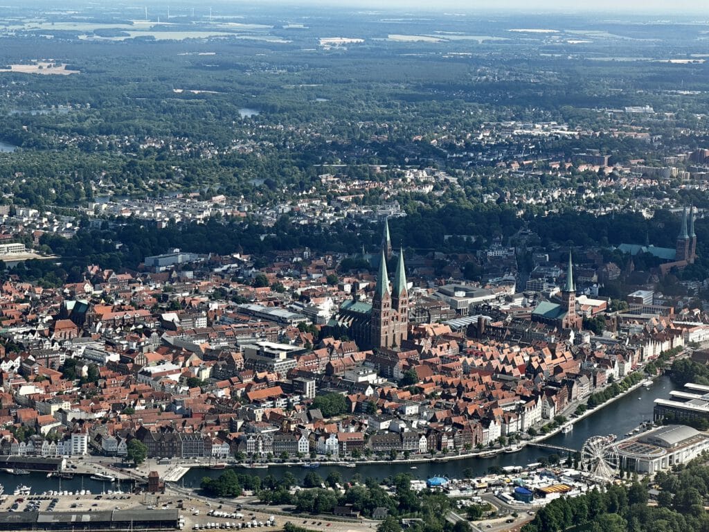 Hansestadt Lübeck während eines Rundfluges. Das Erlebnis floegt gerade an der Stadtinsel vorbei. Der Himmel ist Blau ohne Wolken.