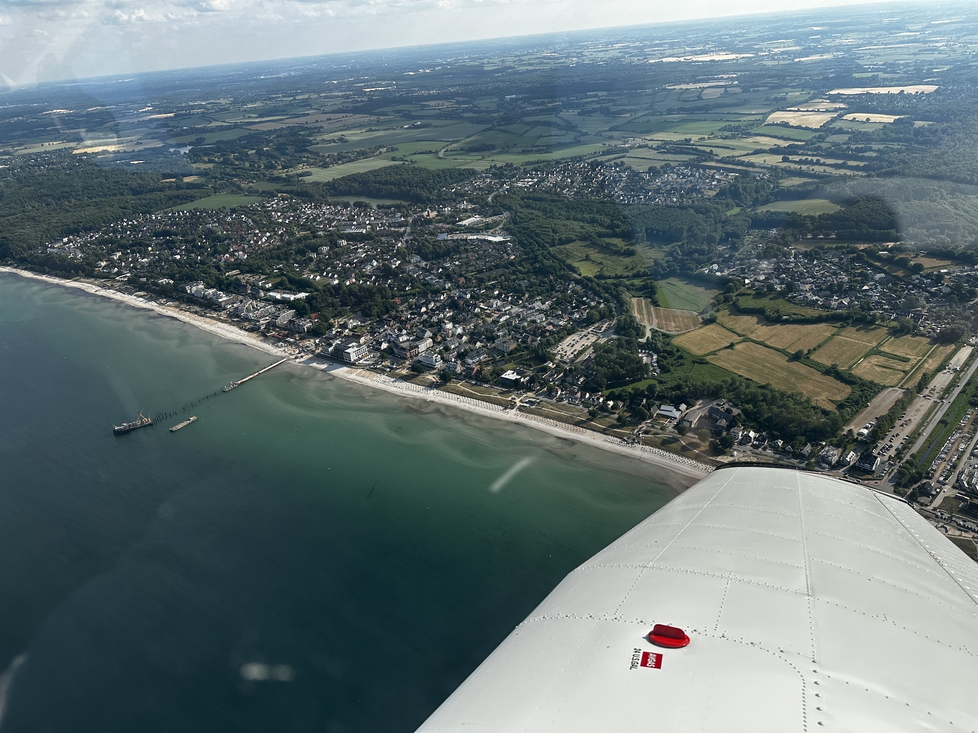 Rundflug über Grömitz und Timmendorfer Strand mit Tragfläche einer Piper PA28. Das Wasser der Bucht ist blau-grün.